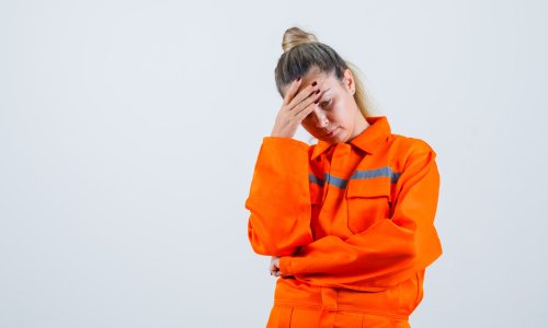 Young female looking at down while holding hand on head in worker uniform and looking upset. front view. space for text